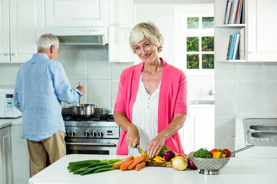 Portrait of happy senior woman cutting vegetables in kitchen